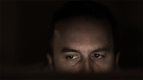 Imagem animada de um rosto no escuro, iluminado apenas pelo que parece ser uma tela de computador. Vê-se os olhos de um lado para o outro e uma gota de suor escorrendo na testa.