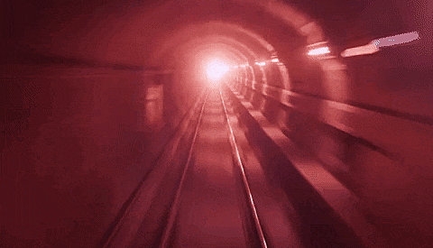 Imagem animada de um túnel subterrâneo, iluminado de vermelho ao fim dos trilhos.