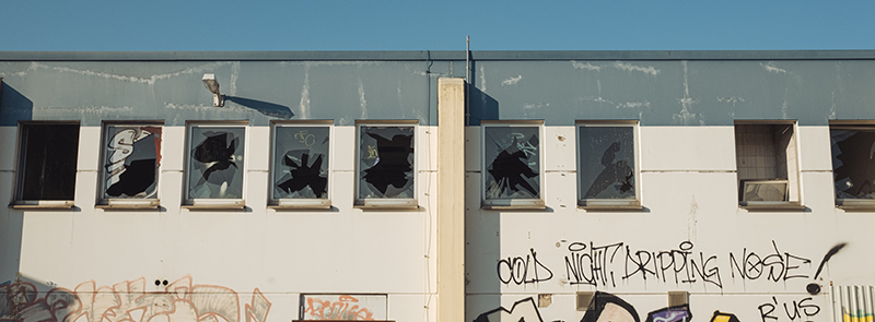 Uma fachada de edificação com várias janelas com os vidros quebrados e graffiti nas paredes.