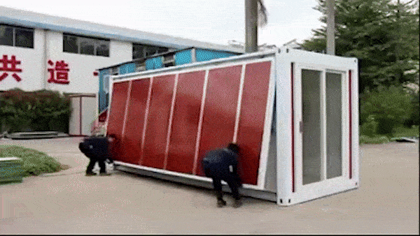 Homens desdobrando uma grande caixa metálica, que se transforma em uma casa. 