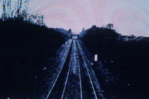 Imagem com tratamento estilo VHS de dois trilhos de trem em meio a colinas.